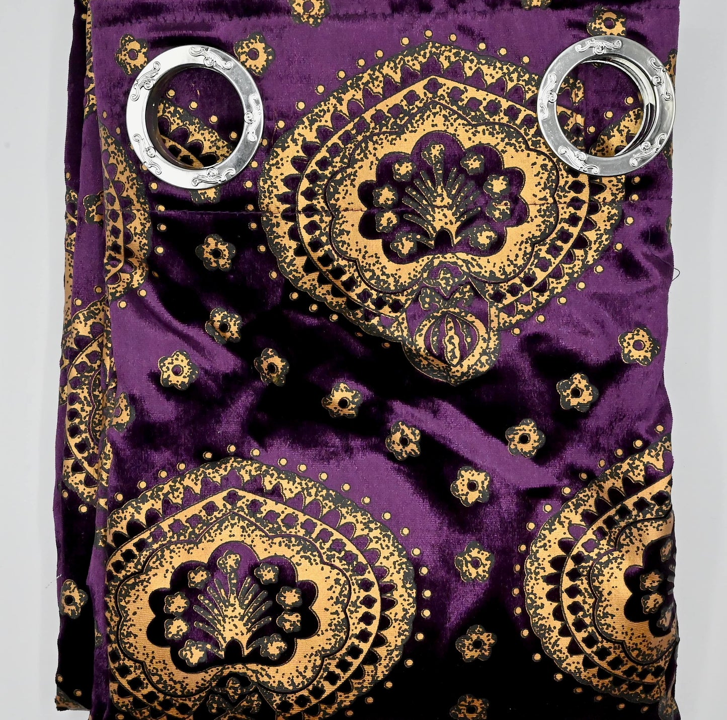 Decorative purple fabric with gold patterns and silver rings on a gray background