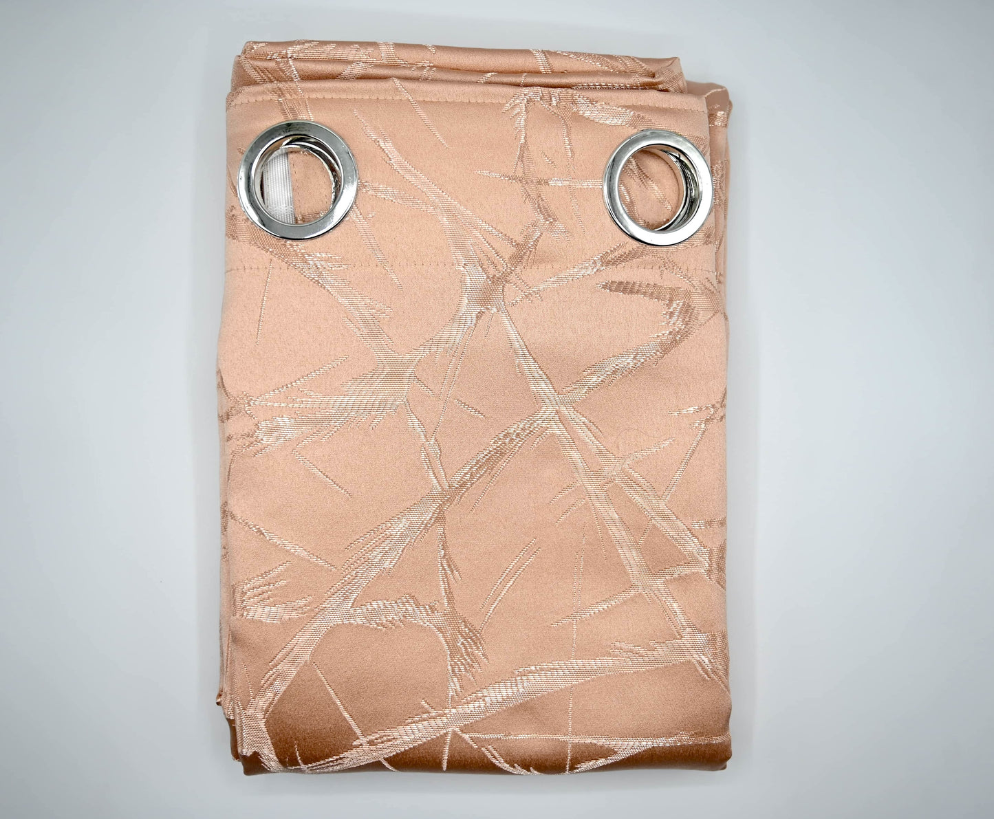 Folded beige curtain with metallic leaf pattern and silver grommets on a light gray background