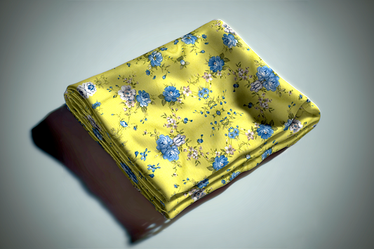Yellow floral curtain fabric with blue roses and botanical print folded on grey surface